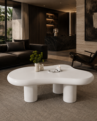A glossy white, organic-shaped coffee table with thick cylindrical legs in a modern, dark-toned living room setting.