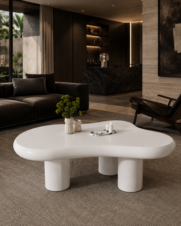 A glossy white, organic-shaped coffee table with thick cylindrical legs in a modern, dark-toned living room setting.