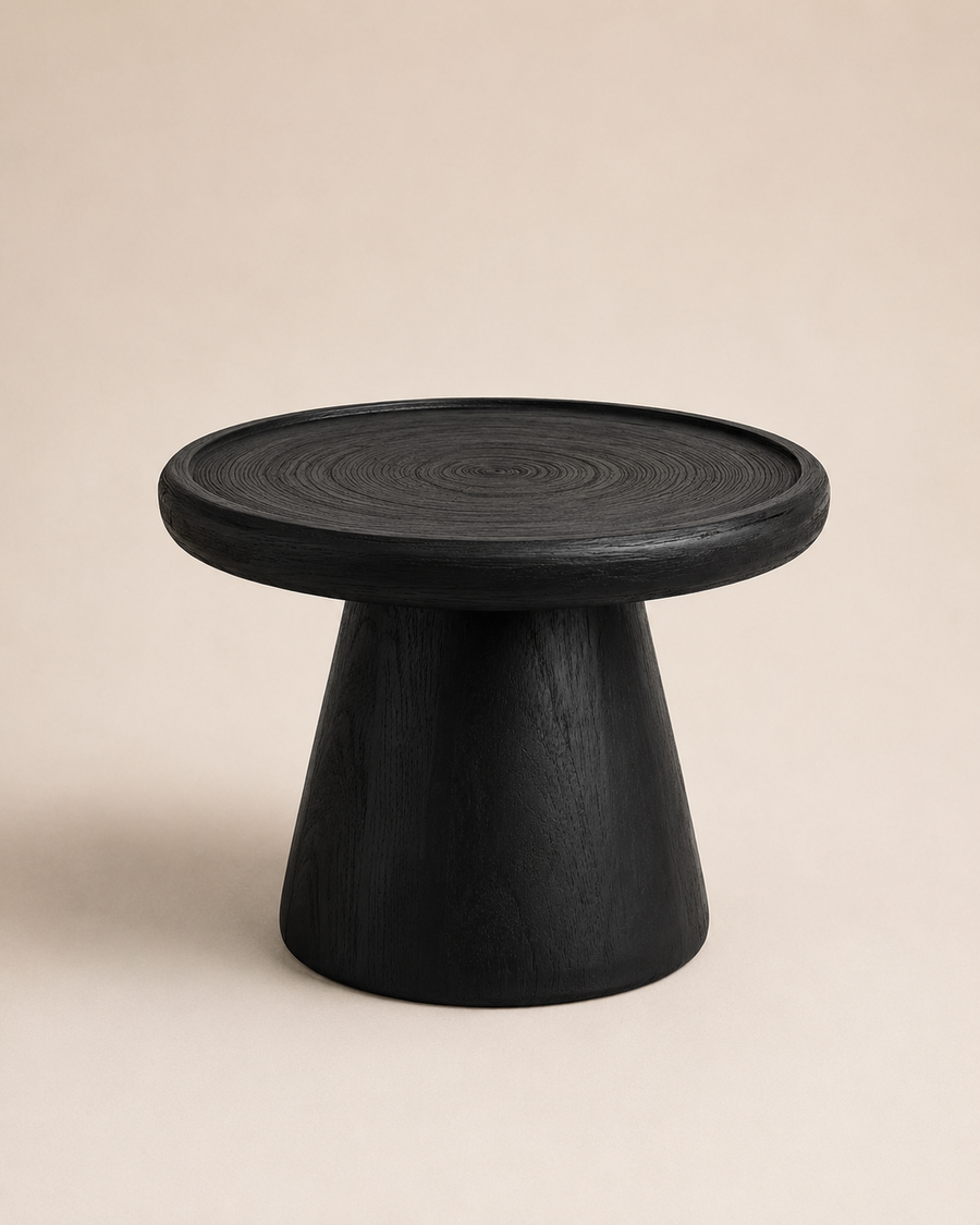 A minimalist black wooden side table with a circular top and tapered pedestal base, photographed against a solid warm beige background.