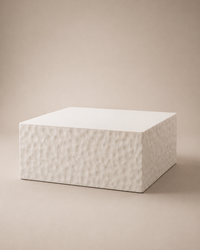 A square white pedestal or block with a textured, hammered surface on the front and smooth top, set against a solid beige background.
