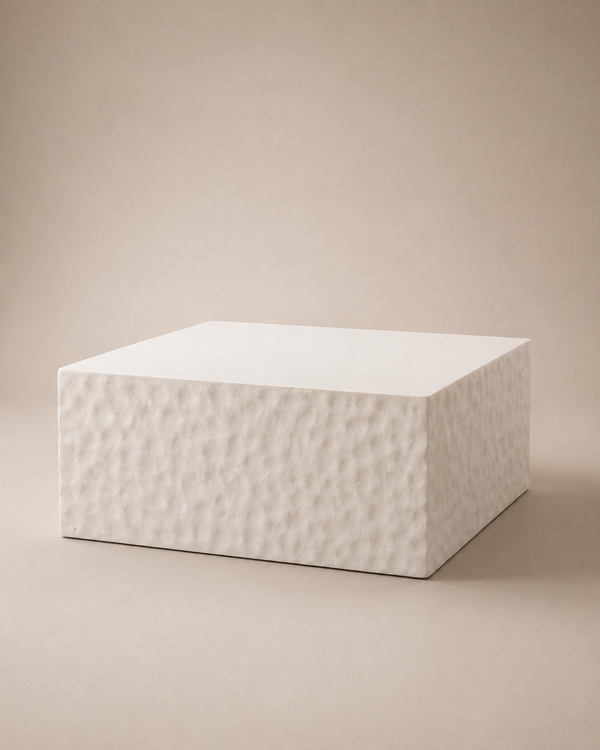 A square white pedestal or block with a textured, hammered surface on the front and smooth top, set against a solid beige background.