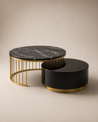 Two modern nesting coffee tables on a warm beige studio background. The larger table has a black marble top with white veining and a gold metal frame, while the smaller table is glossy black with a gold base.