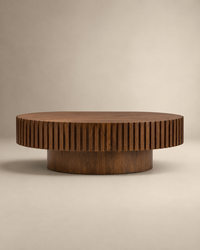 A round wooden coffee table with a fluted, ribbed outer edge and a cylindrical base, shown on a neutral beige studio background.