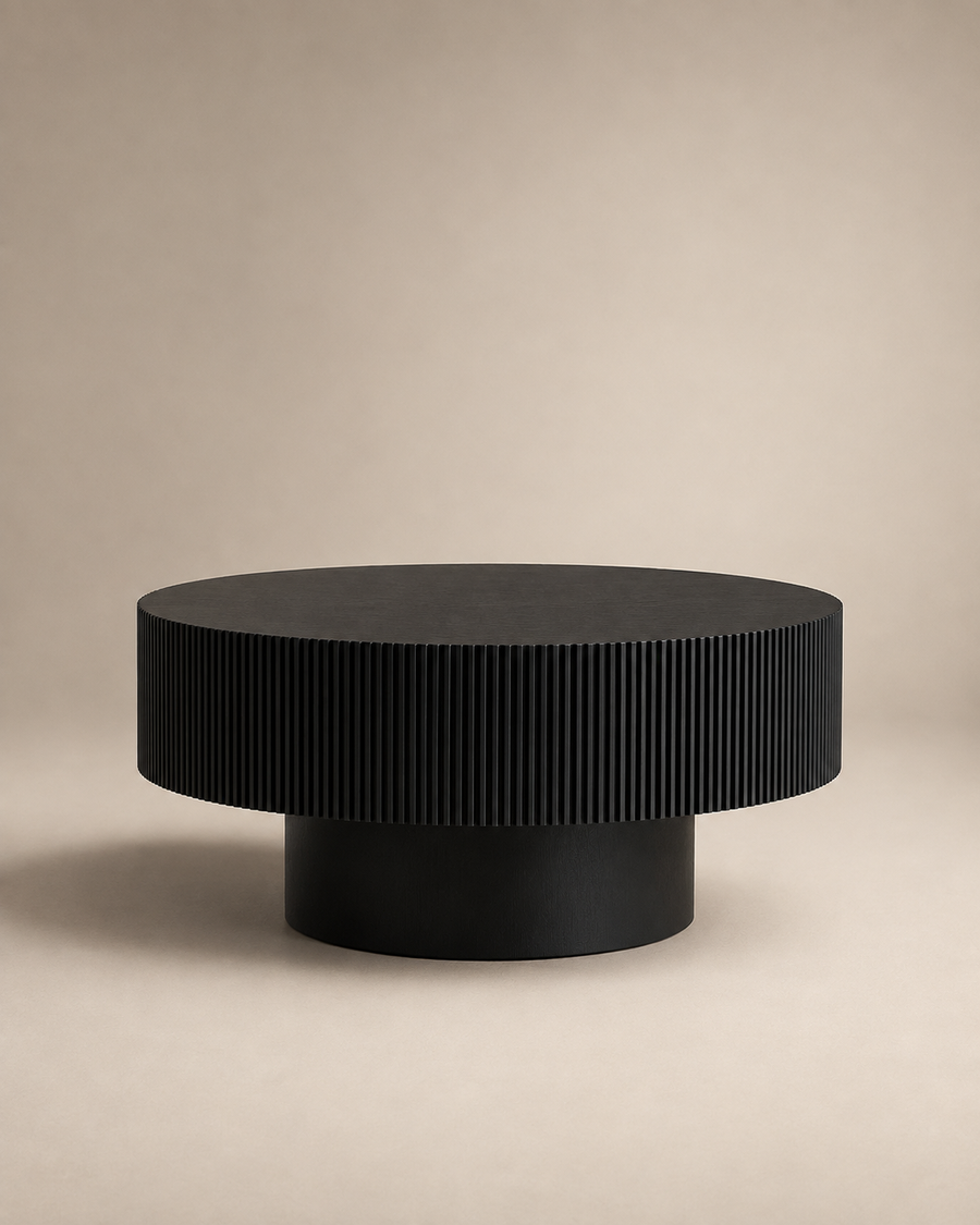 A modern round coffee table with a black ribbed fluted top and a cylindrical black pedestal base, set against a warm beige studio background.