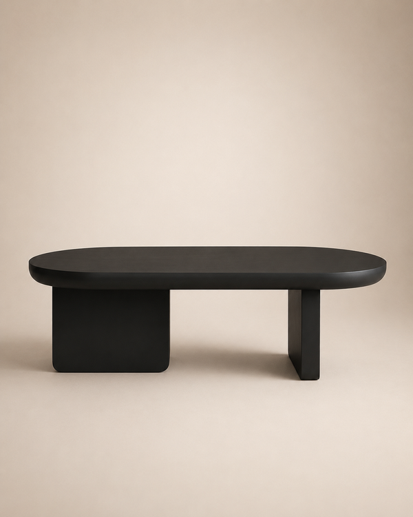 A minimalist black oval coffee table with a thick block base and a single angled leg, shown against a solid beige background.