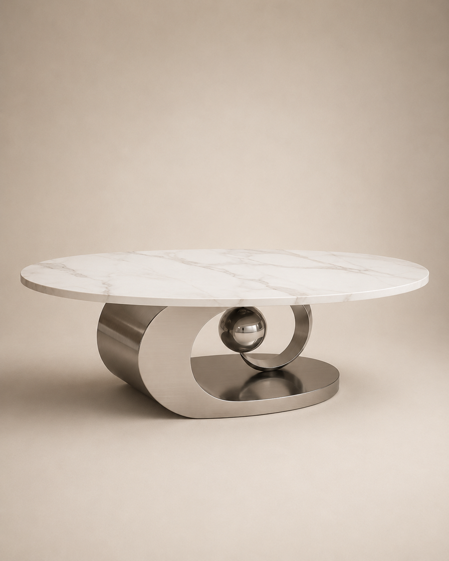 A modern round coffee table with a white marble top and a sculptural brushed metal base featuring a central polished sphere, set against a warm beige background.