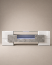 A modern low-profile media console with a glossy white high-gloss finish, textured gray stone-look front panels, and a glass top shelf illuminated by blue LED lighting, set against a neutral beige background.