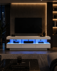 A modern white floating TV console with built-in blue LED under-glow, styled in a contemporary living room setting with a large black TV mounted on a dark textured wall.