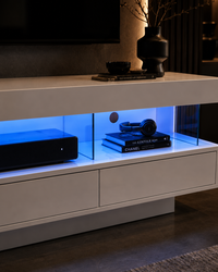 A modern white floating media console with glass-front shelves illuminated by blue LED lighting, styled in a contemporary living room setting.