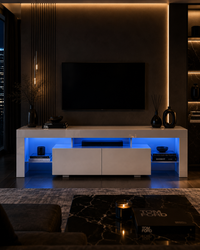 A modern white floating TV console with blue LED under-glow, set in a dark living room with a wall-mounted TV and warm ambient lighting.