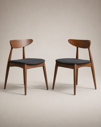 Two mid-century modern wooden dining chairs with dark gray upholstered seats, shown side by side against a warm beige studio background.