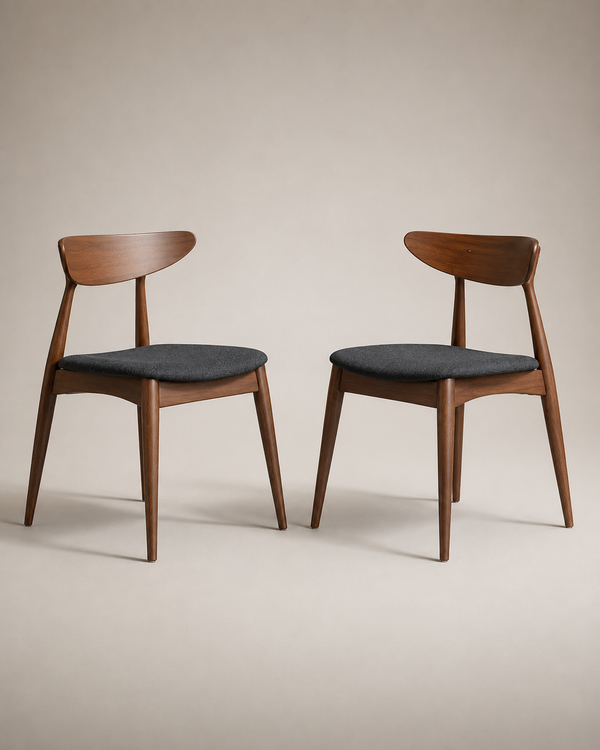 Two mid-century modern wooden dining chairs with dark gray upholstered seats, shown side by side against a warm beige studio background.
