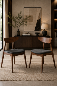 Two mid-century modern wooden dining chairs with dark gray upholstered seats, positioned in front of a dark wood credenza in a styled dining room setting.