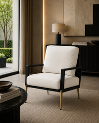 A modern accent chair with a white upholstered seat and back cushion, a black frame, and gold-toned legs, shown in a styled interior room setting.