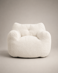 A plush, rounded armchair upholstered in a textured bouclé fabric, shown from the front against a neutral warm gray studio background.