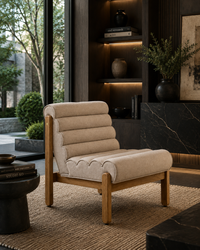 A modern accent chair with a beige ribbed fabric seat and backrest on a light wood frame, styled in a contemporary, dark-toned living room setting.