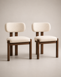 Two modern dining chairs with cream bouclé upholstered seats and rounded backs, supported by dark brown wooden frames, shown against a neutral beige studio background.