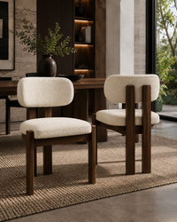 Two modern dining chairs with cream bouclé seats and backs and dark wood frames, placed on a woven rug in a styled dining room setting.