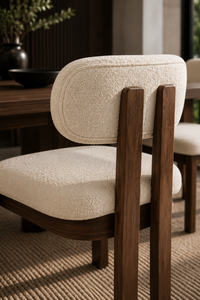 A close-up of a modern dining chair with textured cream bouclé upholstery and dark brown wooden legs, shown in a styled dining room setting.