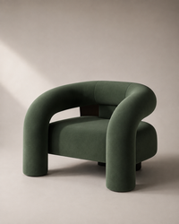 A modern curved armchair upholstered in dark green velvet, set against a minimalist beige studio background with soft diagonal shadows.