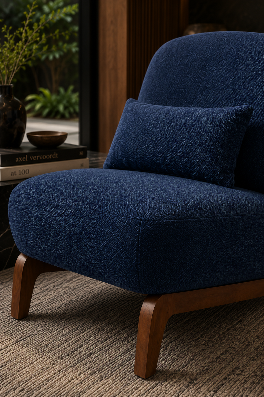 A close-up of a modern armchair upholstered in deep navy blue textured fabric, with a matching square throw pillow and curved wooden legs, set in a styled interior room.