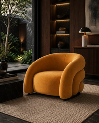 A modern, rounded barrel-style armchair upholstered in a warm mustard-yellow velvet fabric, styled in a luxurious contemporary living room with dark wood cabinetry, a textured rug, and ambient lighting.