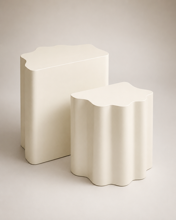 Two modern side tables in a warm off-white finish, one rectangular and one scalloped, photographed on a neutral light beige background.