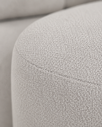 Close-up of a light gray textured fabric upholstery, showing the weave detail and curved seam on a sofa or chair.