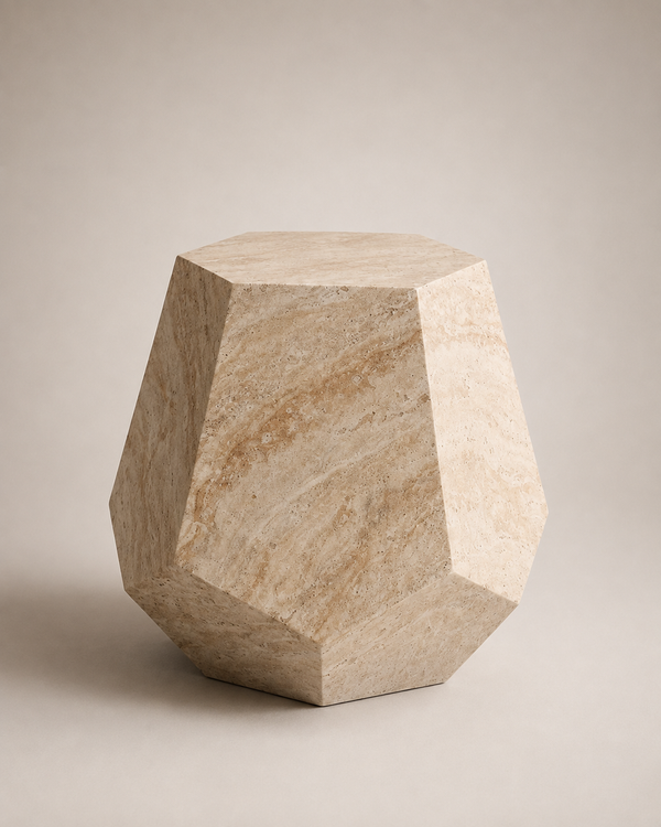 A faceted geometric side table made of light beige travertine stone, photographed on a neutral warm gray studio background.
