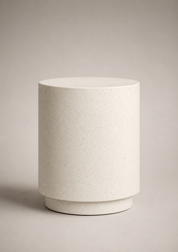 A minimalist cylindrical side table or lamp in a light beige speckled stone or concrete finish, set against a neutral warm gray background.