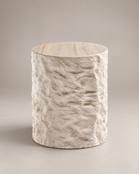 A cylindrical side table with a textured, stone-like beige and cream finish, shown on a neutral warm gray background.