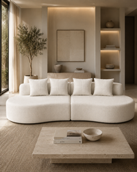 A modern curved modular sofa upholstered in warm off-white bouclé fabric, styled in a minimalist, warm-toned living room with a matching coffee table and neutral decor.