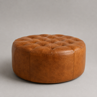 Round tufted leather ottoman in a warm cognac brown, photographed on a neutral gray studio background.