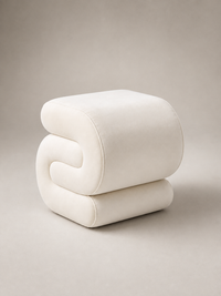 A modern sculptural ottoman or stool in a soft off-white velvet fabric, featuring a stacked, curved design, photographed on a neutral warm gray studio background.