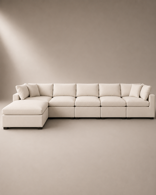 A modern sectional sofa with a left-facing chaise lounge, upholstered in a warm off-white fabric, set against a minimalist beige studio background.