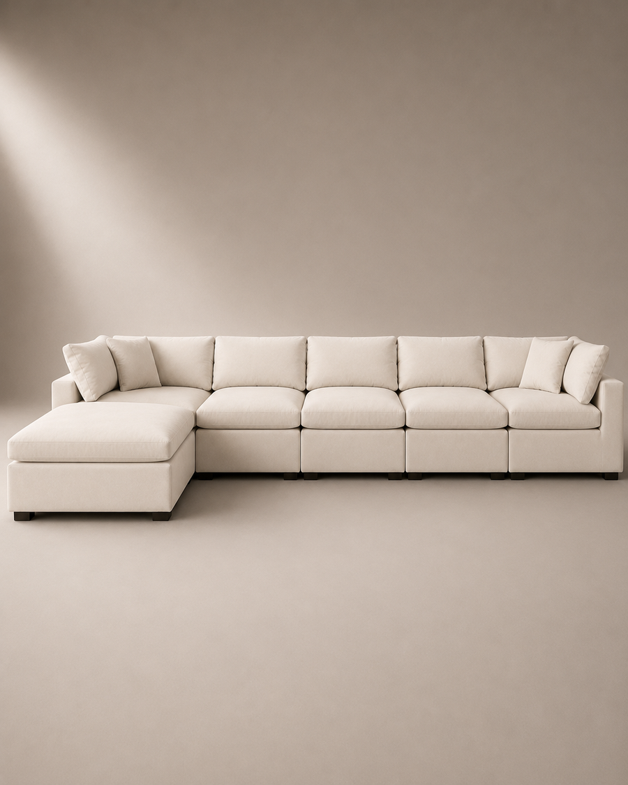 A modern sectional sofa with a left-facing chaise lounge, upholstered in a warm off-white fabric, set against a minimalist beige studio background.