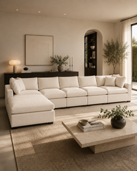 A modern sectional sofa in off-white upholstery arranged in a spacious, minimalist living room with a matching textured rug, a low stone coffee table, and warm ambient lighting.