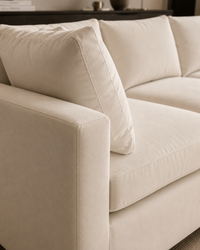 Close-up of a cream or off-white upholstered sofa with thick cushions and a rounded armrest, shown in a softly lit interior setting.