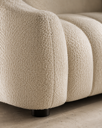 Close-up of a textured bouclé sofa arm in warm off-white, showing the looped fabric detail and a small dark round foot.