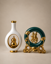 Two decorative home decor sculptures on a beige background: a white vase with a gold gourd motif and a dark green circular plaque with a gold Chinese character and ornate gold stand.