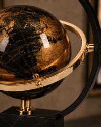 Close-up of a decorative globe with a black and gold map design, mounted on a black stand with a gold ring and curved black support arm.