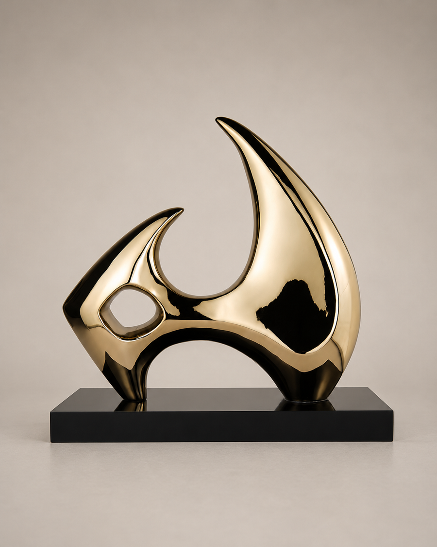 A modern abstract sculpture with a glossy metallic gold finish and a black rectangular base, photographed against a neutral light gray background.