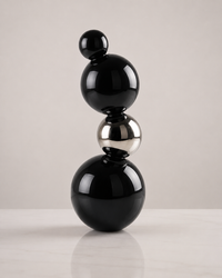 A modern abstract sculpture made of stacked glossy black and polished silver metallic spheres on a light gray background.