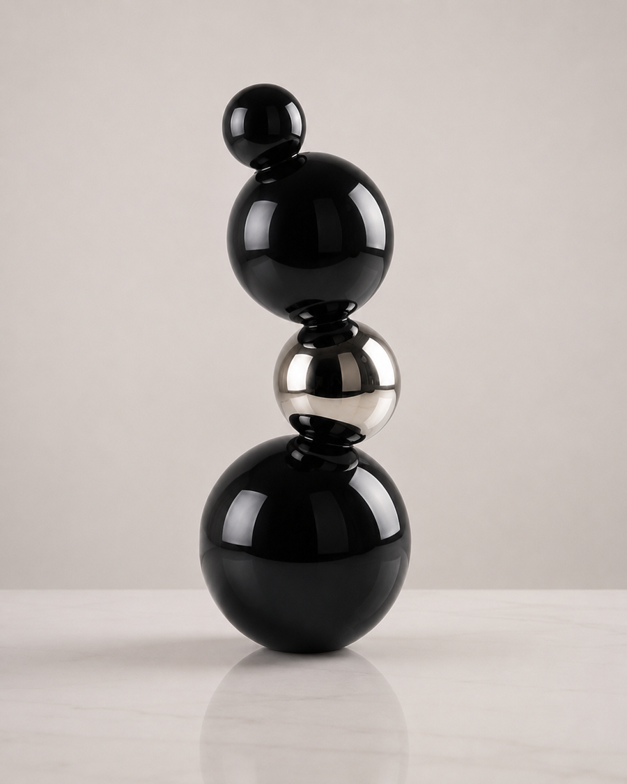 A modern abstract sculpture made of stacked glossy black and polished silver metallic spheres on a light gray background.