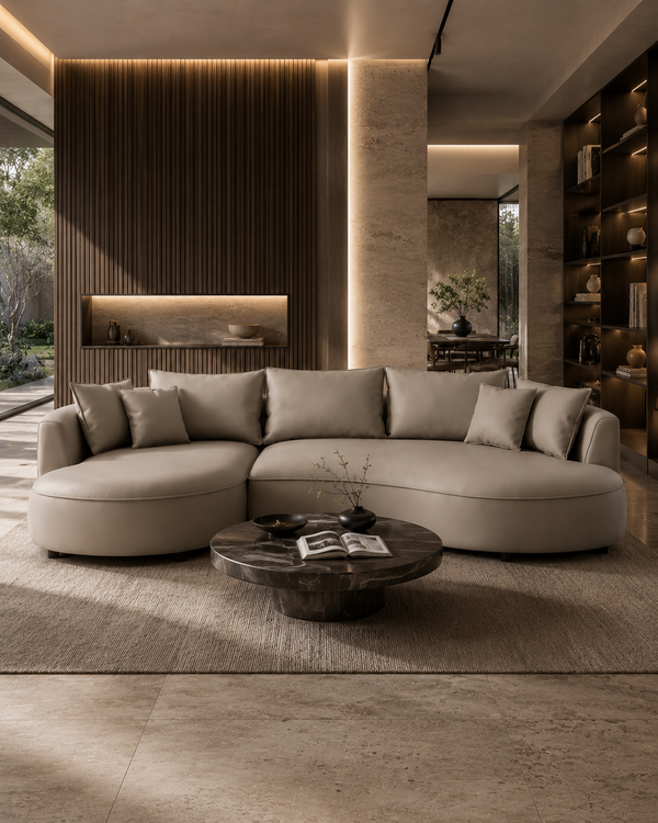 A modern curved sectional sofa upholstered in light beige fabric, styled in a luxurious contemporary living room with a dark wood coffee table and warm ambient lighting.