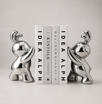 Two shiny silver elephant bookends holding a set of four white books with black text, photographed on a clean light gray background.