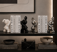 Decorative bookends displayed on a dark shelf in a modern interior setting. The set includes four sculptural rabbit figures in matte white, matte black, and metallic silver finishes, flanking books with 'IDEA ALPH' and 'KNIFOLK' titles.