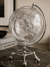 A vintage-style globe with a transparent globe罩 and silver metal stand, displayed on a dark marble surface with a book in the background.