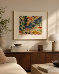 A framed abstract landscape painting with vibrant green, blue, red, and yellow brushstrokes, displayed on a beige wall above a dark wood sideboard in a styled living room setting.