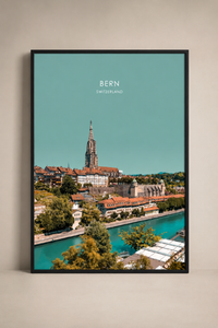 A framed vertical art print of Bern, Switzerland, featuring a turquoise sky and cityscape with the cathedral spire and river, displayed on a neutral beige wall.
